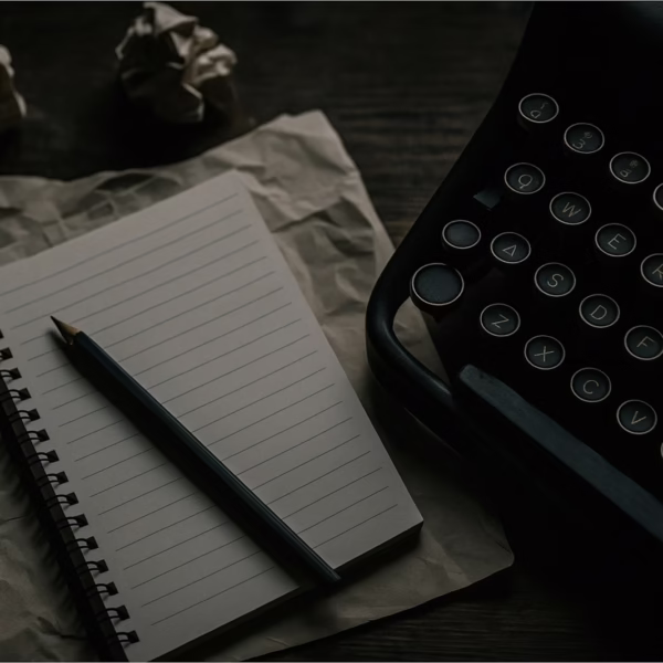 A typewriter, notepad, and crumpled paper are shown.