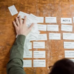 A person arranging storyboard cards on a wooden table for a film script planning session.